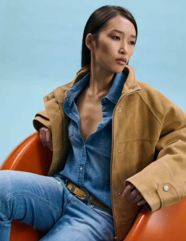 Model im camelfarbenen Wildlederblouson über Jeanshemd und Jeans, sitzend in einem orangefarbenen Sessel